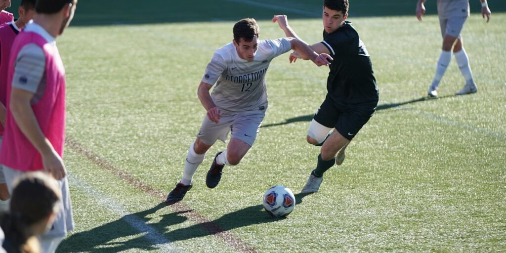 Two footballers contesting the ball on a grass pitch