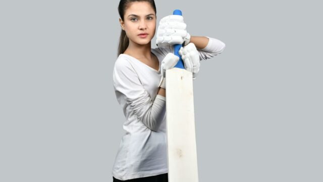 A woman cricketer in whites holding a bat