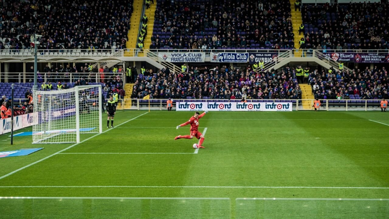 A footballer on a stadium pitch with the goal behind