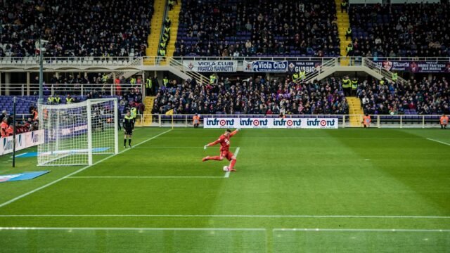 A footballer on a stadium pitch with the goal behind